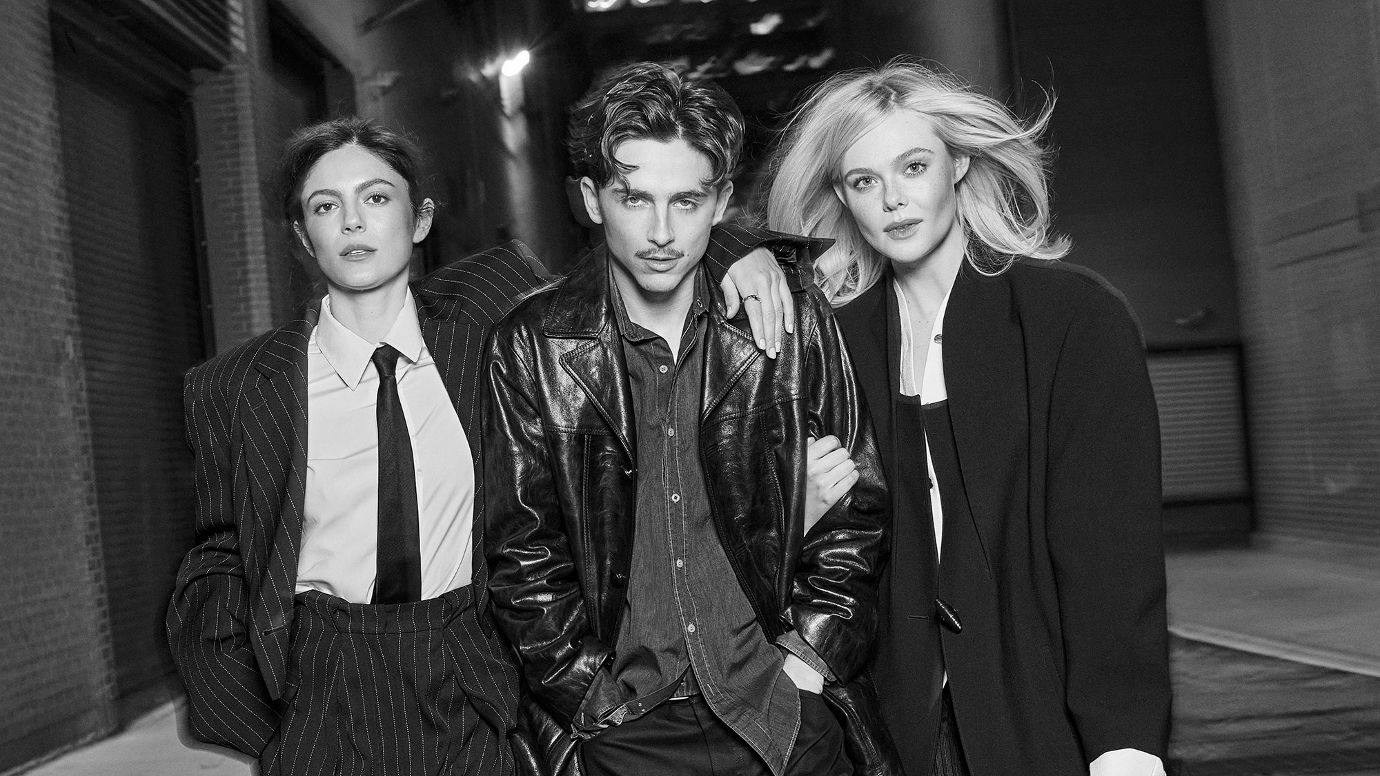 Timothee Chalamet, Elle Fanning and Monica Barbaro were photographed in New York City on November 23rd 2024. Monica, left, Sportmax pinstripe jacket, white shirt, pants; Turnbull and Asser silk tie; Bulgari ring; Christian Louboutin boots. Hair by Jacob Rosenberg, Makeup by Samantha Lau Timothee, center, Celine leather jacket, jeans, boots; CK vintage shirt. Styling by Taylor McNeill, Grooming by Jamie Taylor. Elle, right, Louis Vuitton coat, shirt dress, skirt; Gianvito Rossi boots. Hair by Alissa Frum, Makeup by Tyron Machhausen Artistic and Fashion Director Alison Edmond